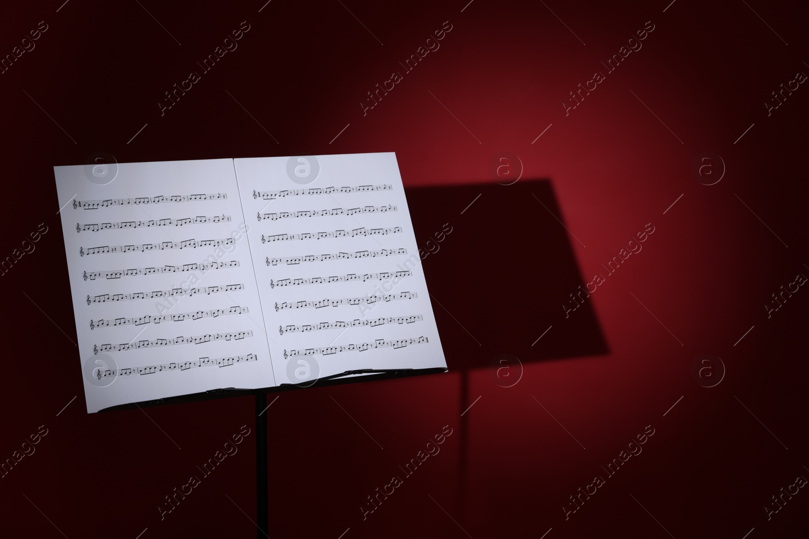 Note stand with music sheets on dark red background, space for text Photo of Note stand with music sheets on dark red background, space for text