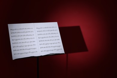 Photo of Note stand with music sheets on dark red background, space for text