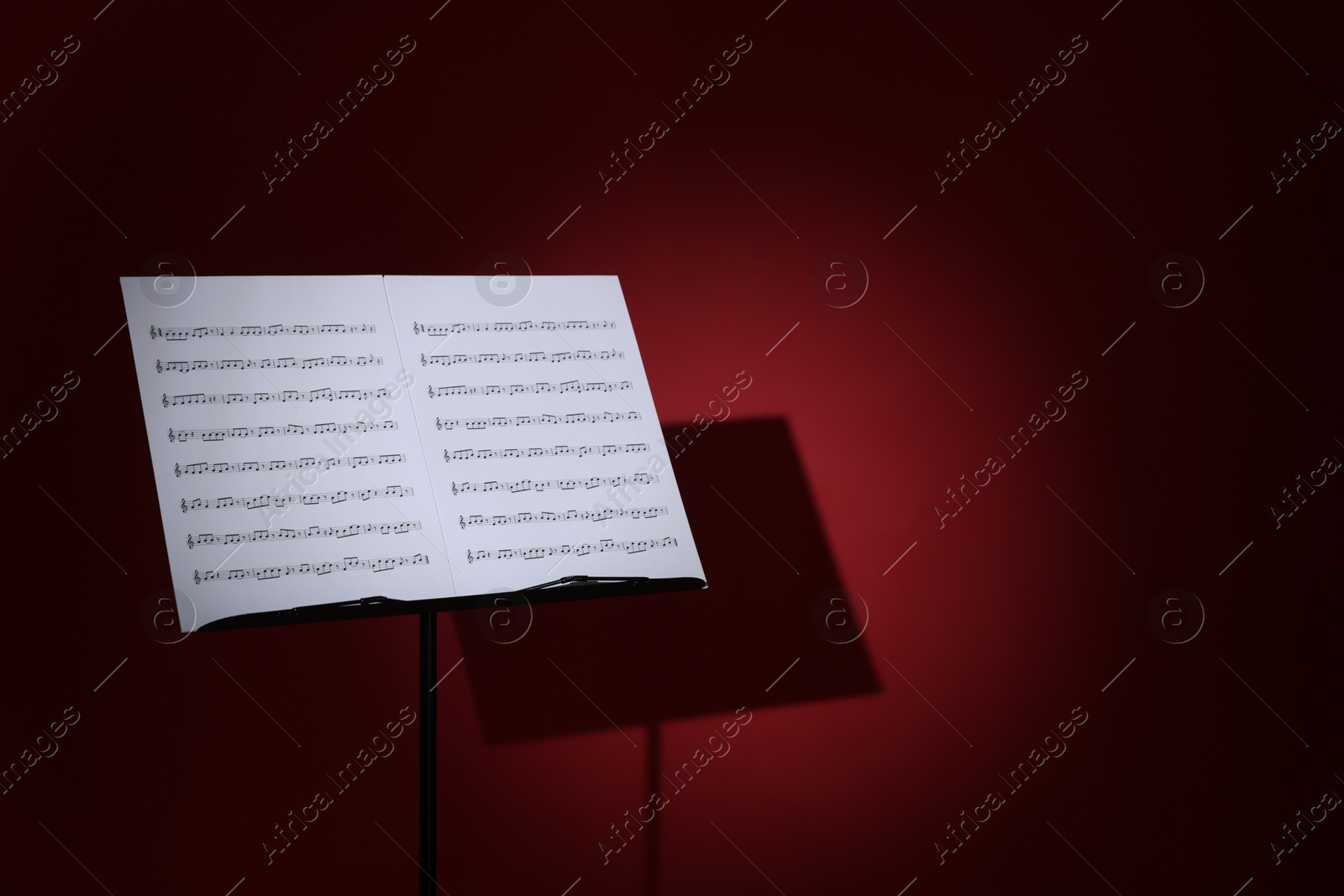 Note stand with music sheets on dark red background, space for text Photo of Note stand with music sheets on dark red background, space for text