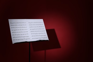 Photo of Note stand with music sheets on dark red background, space for text