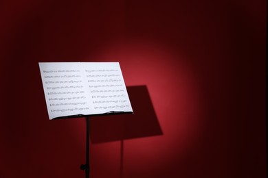 Photo of Note stand with music sheets on dark red background, space for text