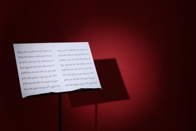 Photo of Note stand with music sheets on dark red background, space for text