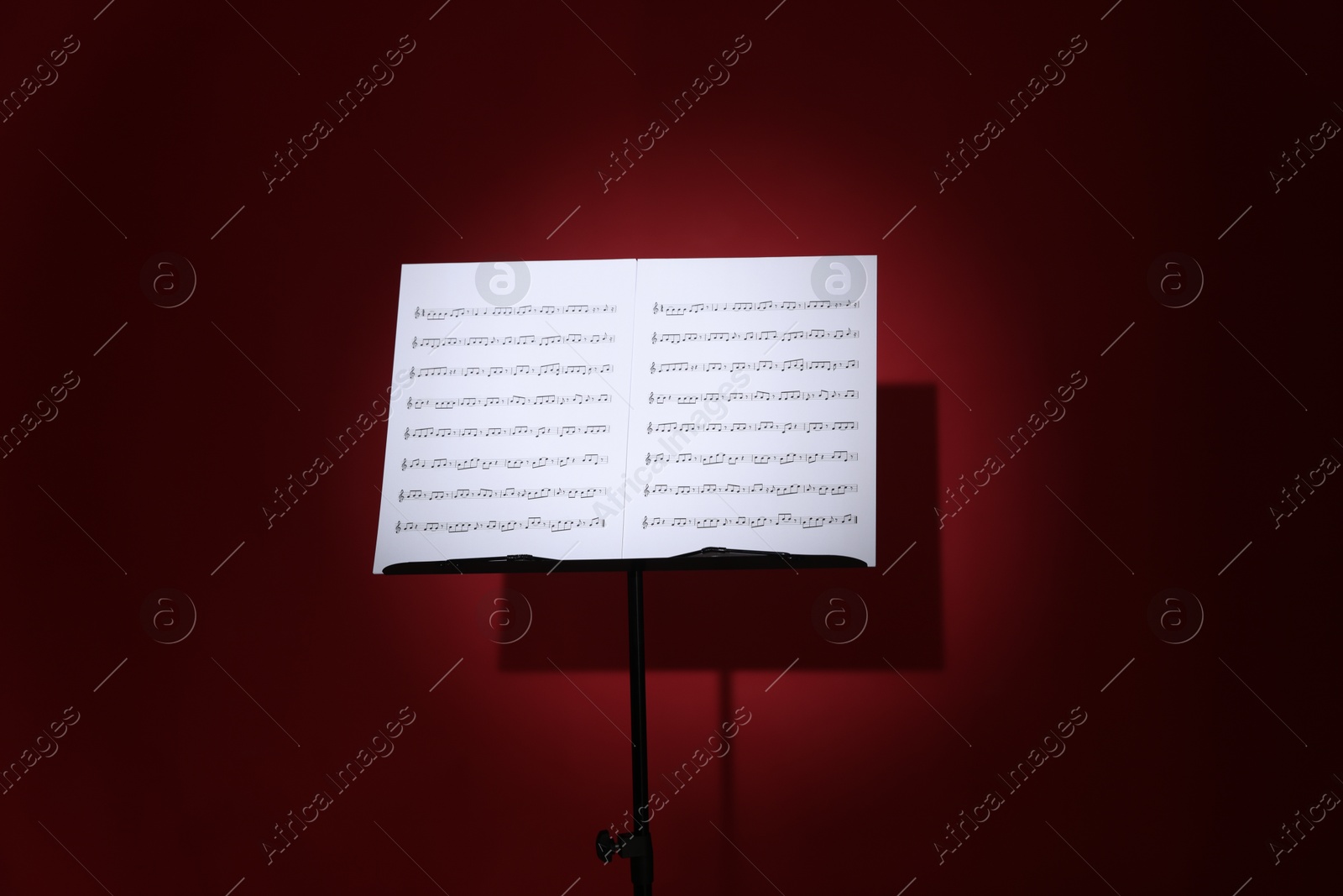 Note stand with music sheets on dark red background Photo of Note stand with music sheets on dark red background