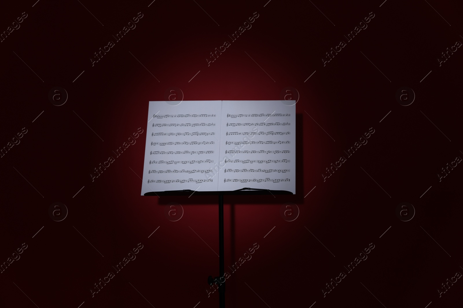 Note stand with music sheets on dark red background Photo of Note stand with music sheets on dark red background