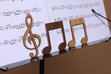 Photo of Stand with music sheets and wooden notes on dark beige background, closeup