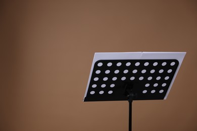 Photo of Stand with music sheets on dark beige background, space for text