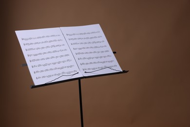 Photo of Stand with music sheets on brown background, space for text