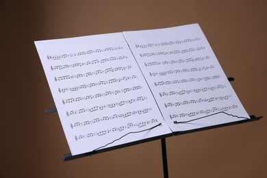 Photo of Stand with music sheets on brown background, closeup