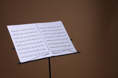 Photo of Stand with music sheets on brown background, space for text