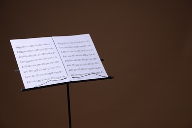 Photo of Stand with music sheets on brown background, space for text