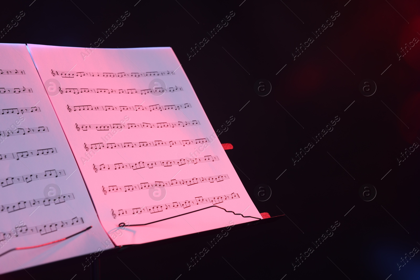 Stand with music sheets in neon lights on dark background, closeup. Space for text Photo of Stand with music sheets in neon lights on dark background, closeup. Space for text