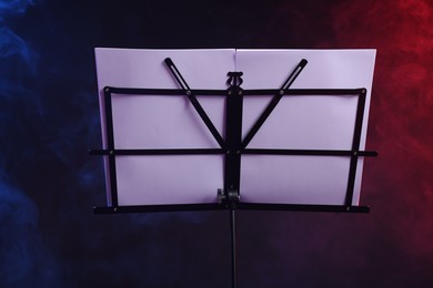 Photo of Stand with music sheets on dark background with smoke