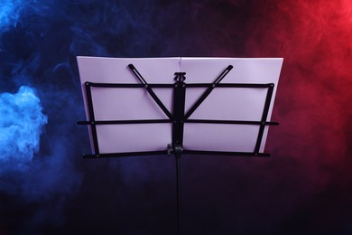 Photo of Stand with music sheets on dark background with smoke