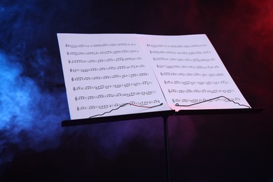 Photo of Stand with music sheets on dark background with smoke, closeup