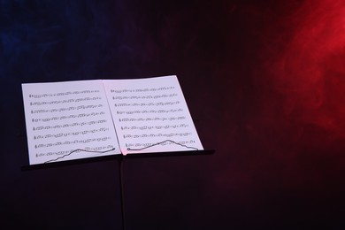 Photo of Stand with music sheets on dark background with smoke, space for text