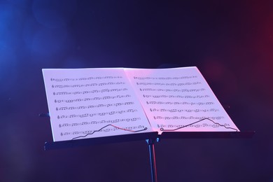 Photo of Stand with music sheets in neon lights on dark background, closeup