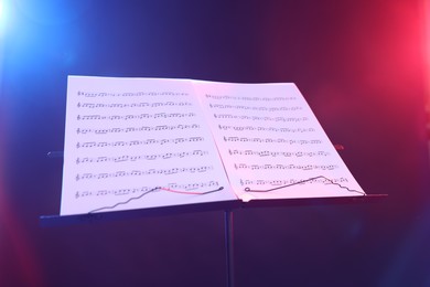 Photo of Stand with music sheets in neon lights on dark background, closeup