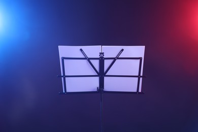 Photo of Stand with music sheets in neon lights on dark background