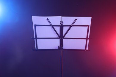 Photo of Stand with music sheets in neon lights on dark background