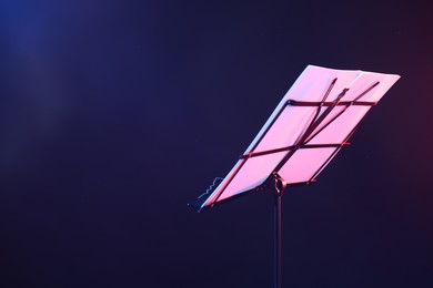Photo of Stand with music sheets in neon lights on dark background, closeup. Space for text