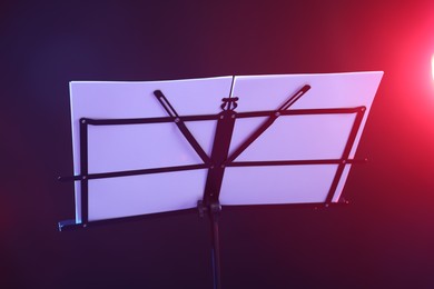 Photo of Stand with music sheets in neon lights on dark background, closeup