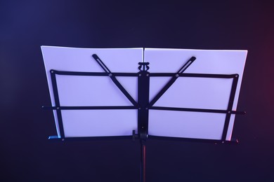 Photo of Stand with music sheets in neon lights on dark background, closeup