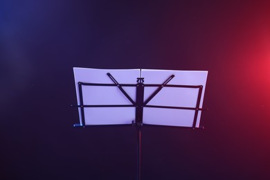Photo of Stand with music sheets in neon lights on dark background