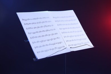 Photo of Stand with music sheets in neon lights on dark background, closeup