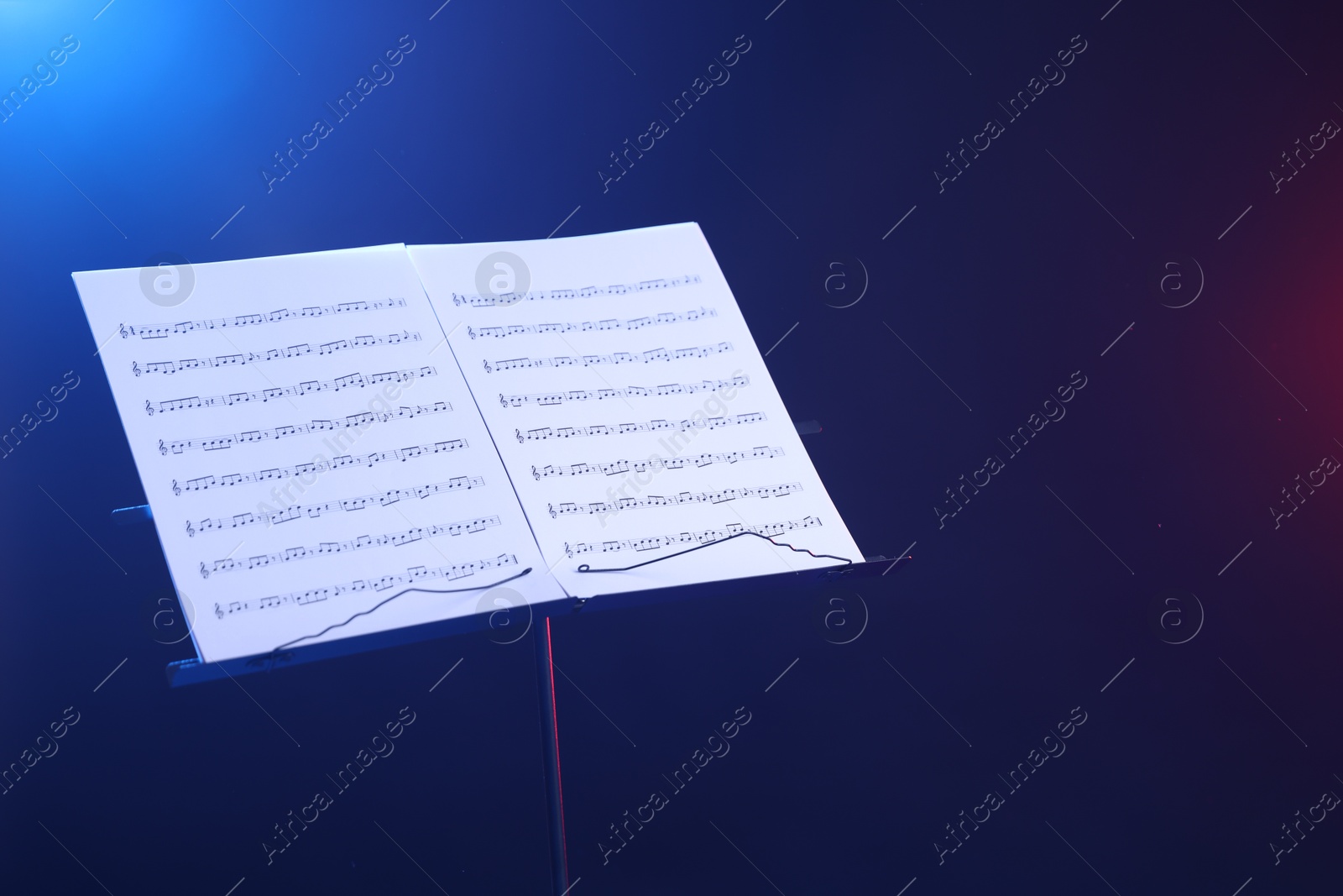 Stand with music sheets in neon lights on dark background, space for text Photo of Stand with music sheets in neon lights on dark background, space for text