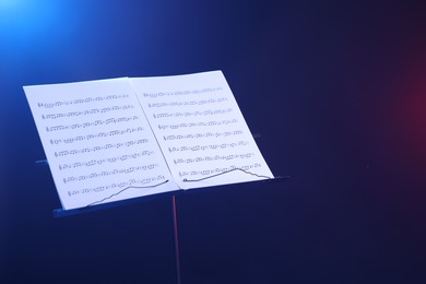 Photo of Stand with music sheets in neon lights on dark background, space for text