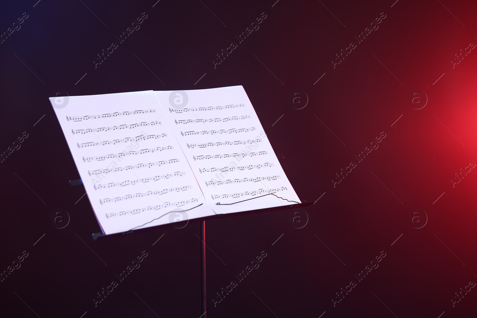 Stand with music sheets in neon lights on dark background, space for text Photo of Stand with music sheets in neon lights on dark background, space for text