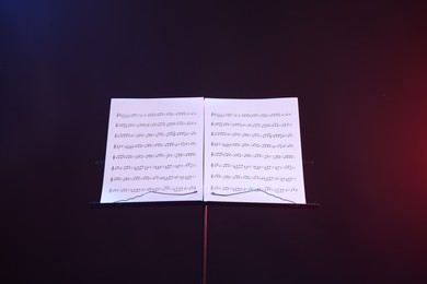 Photo of Stand with music sheets in neon lights on dark background