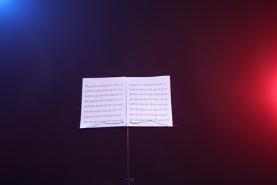 Photo of Stand with music sheets in neon lights on dark background