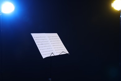Photo of Stand with music sheets on dark background, space for text