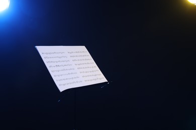 Photo of Stand with music sheets on dark background, space for text