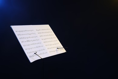 Photo of Stand with music sheets on dark background, space for text