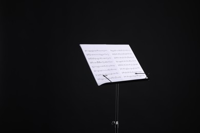 Photo of Stand with music sheets on black background, space for text