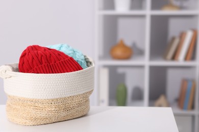 Photo of Different wool hats in wicker basket on white table indoors, space for text