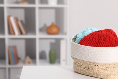 Photo of Different wool hats in wicker basket on white table indoors, space for text