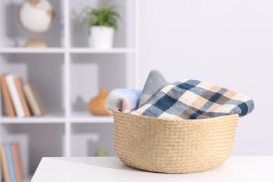 Photo of Stylish wool scarves in wicker basket on white table indoors