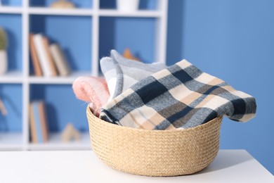 Photo of Stylish wool scarves in wicker basket on white table indoors