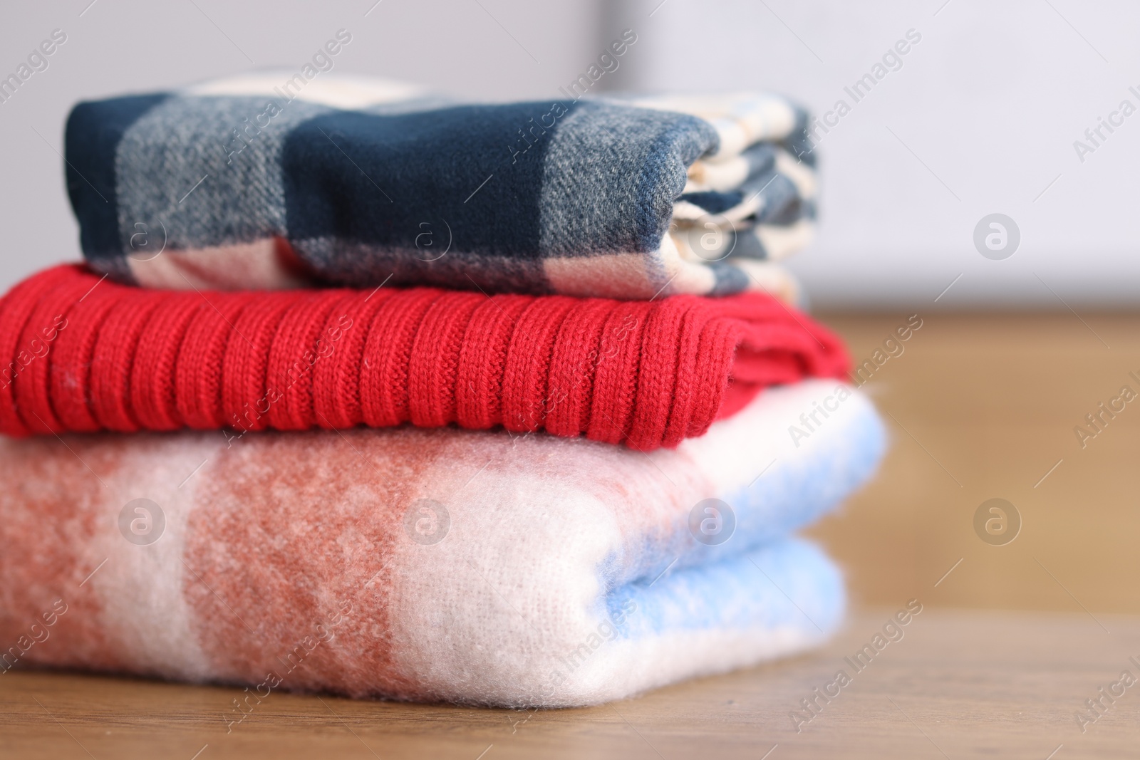 Folded wool sweaters and scarf on wooden table indoors, closeup Photo of Folded wool sweaters and scarf on wooden table indoors, closeup