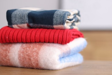 Photo of Folded wool sweaters and scarf on wooden table indoors, closeup