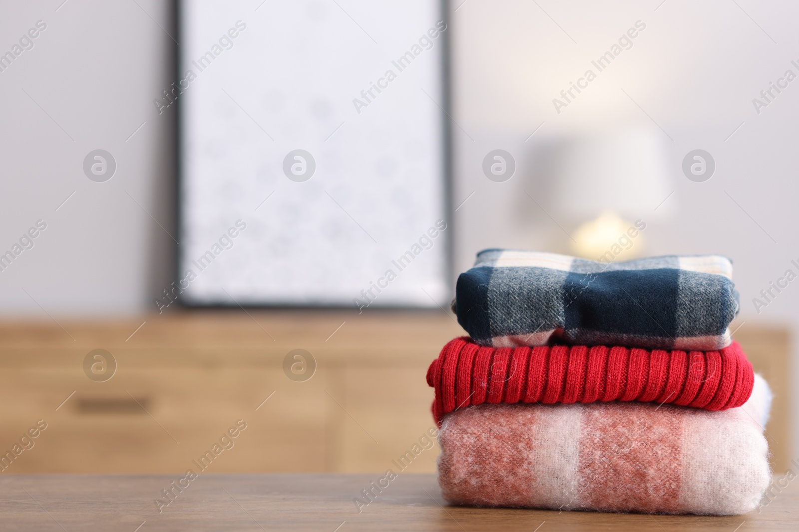 Folded wool sweaters and scarf on wooden table indoors, space for text Photo of Folded wool sweaters and scarf on wooden table indoors, space for text