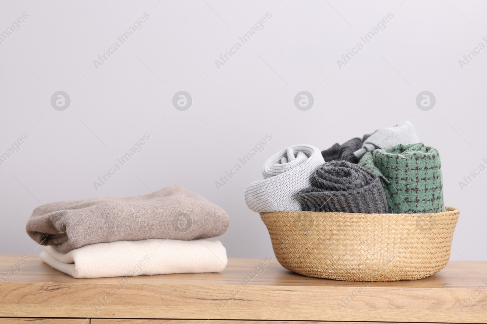 Folded wool sweaters and scarves in wicker basket on wooden table indoors Photo of Folded wool sweaters and scarves in wicker basket on wooden table indoors