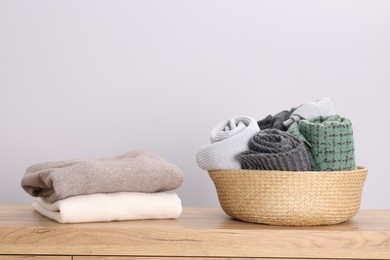 Photo of Folded wool sweaters and scarves in wicker basket on wooden table indoors