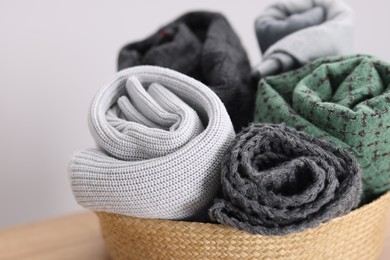 Photo of Wool scarves in wicker basket on light background, closeup