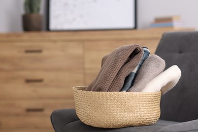Photo of Wool clothes in wicker basket on armchair indoors