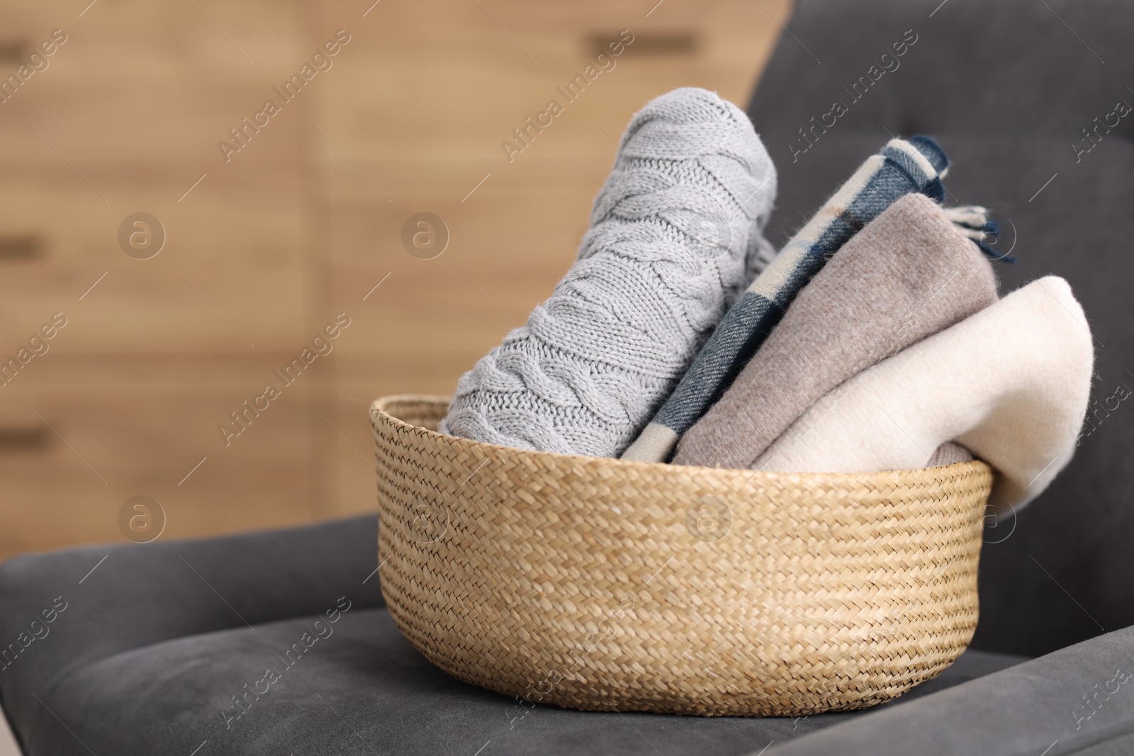 Wool clothes in wicker basket on armchair indoors Photo of Wool clothes in wicker basket on armchair indoors