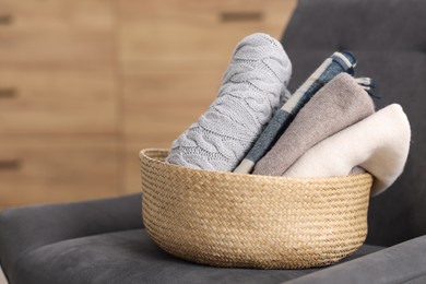 Photo of Wool clothes in wicker basket on armchair indoors